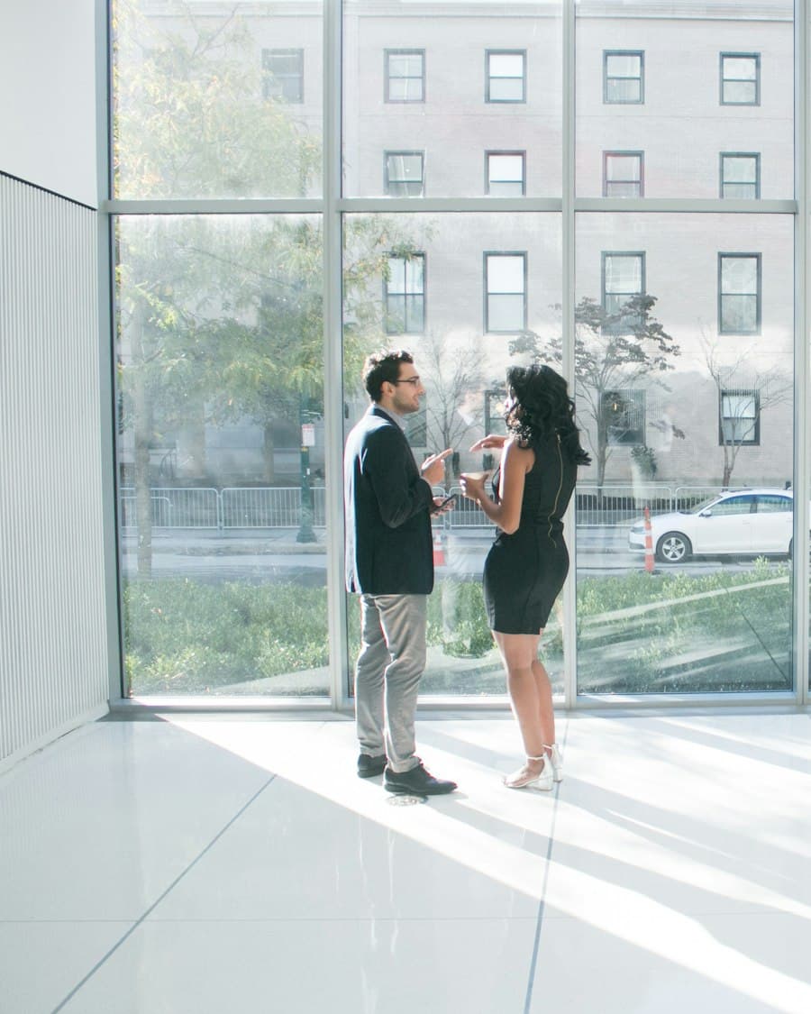 Two people talking beside a full-height window in a bright lobby